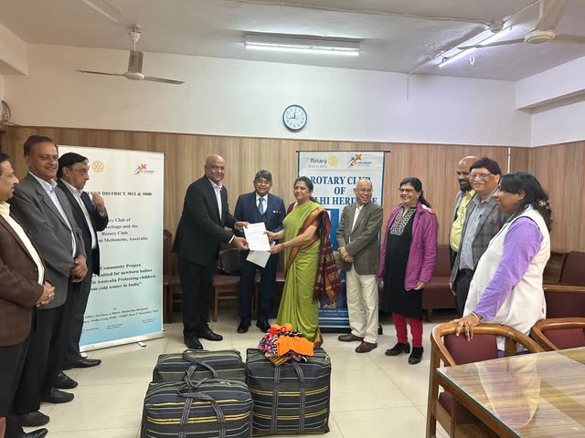 Rotary members, including Rakesh Raizada, holding up hand-knitted baby jumpers