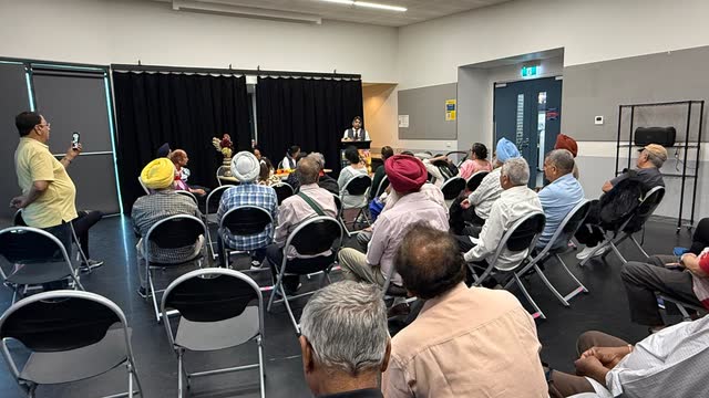 A full room of community members listening to a speaker at a forum
